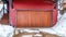 Panorama frame Brown garage door and red wall of home with snowy yard and driveway in winter