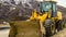 Panorama Front of a yellow bulldozer against snowy mountain and cloudy sky in winter