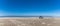 Panorama of a gray camper van parked on an endless white sand beach in the middle of nowhere with ocean behind