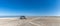 Panorama of a gray camper van parked on an endless white sand beach in the middle of nowhere with ocean behind