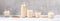 Panorama image of row of glass containers with oat milk on white wooden table on grey concrete wall background.