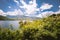 Panorama of a lake with green vegetation around. Natural basin with forest and mountains.