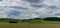 Panorama landscape of rolling hills and fields with a large farmhouse under an expressive sky