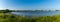 Panorama landscape of a small ocean lagoon with a sandy beach and a wildflower meadow under a blue sky