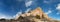 Panorama of a large mountain ridge of exposed, light colored rock against a deep blue sky with clouds