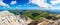 Panorama of a mountain landscape. View from the top of the mountain of crumbling rocks, green mountain pastures and blue