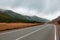 Panorama of mountain road of on background of beautiful snowy mountain peaks in cloudy weather. Mountain highway. View