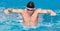 Panorama of Muscular swimmer young man in black cap in swimming pool, performing butterfly stroke.