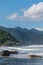 Panorama of a natural environment with the sea waves hitting against wide rocks and a great mountain with tall trees in