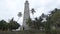 Panorama of palms in tropical forest with small cottages and ancient stone tower against cloudy sky, landmark