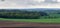 Panorama of plowed and fresh green agricultural fields under a cloudy sky.