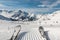 Panorama point of view skier legs on downhill start straight line rows freshly prepared groomed ski slope piste on bright day blue