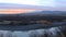 Panorama of a river at dusk with a sunset beyond the distant mountains zoom as the camera pans