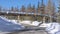 Panorama Road passing under a bridge amid fresh snow and evergreens on a sunny winter day