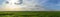 Panorama scene of green grass field with blue cloudy sky.