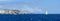 Panorama of the sea and rocks on a Sunny day. Sailing yacht with a white sail, copy space