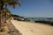 Panorama seascape dayshot of a white yellow sand beach with long boats, palm trees, mountains, turquoise ocean water and a blue