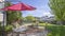 Panorama Seating area on a stone patio under the shade of a red umbrella on a sunny day