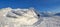 A panorama of snow capped mountains with textured, frozen, mystical fanciful shaped stones, a man in a ski suit.