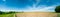 Panorama of summer green field. European rural view. Beautiful landscape of wheat field and green grass with stunning blue sky and
