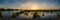 Panorama of sunset landscape over flooded land next to a levee with colorful sky