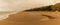 Panorama view of a beautiful long and empty beach with shore break and high sand dunes behind and sahara dust in the air