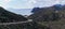 Panorama view of a curvy dirt road leading down to a secluded beach on a wild and mountainous coastline