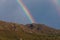 Panorama view of full double rainbow with blue sky and mountain range in background. Near Saint Florent, Corsica