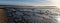 Panorama view of golden evening light reflectiing in tidal pools on a rocky beach with the ocean behind