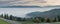 Panorama view of rolling mountain ridges in a light hazy sky with fall color forest and a winding mountain road and train tracks i