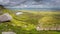 Panorama with view on steep stairs of wooden boardwalk leading to Cuilcagh Mountain peak with lake and valley below