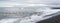 Panorama of waves crash ashore on Hvalnes beach with black lava sand on Hvalnes peninsula in southern Iceland.