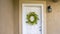 Panorama White front door with green leafy wreath and doormat at the facade of a home