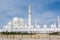 Panorama of White Grand Mosque with fence against blue sky, also called Sheikh Zayed Grand Mosque, inspired by Persian, Mughal and