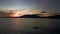 Panoramic aerial view of motor boar sliding along the sea against black silhouette of mountains and hills at sunset