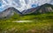 Panoramic alpine landscape with beautiful shallow mountain lake with streams in highland green valley from bigger mountains under