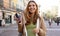 Panoramic banner of confident carefree young woman walking in pedestrian street in old town holding smartphone and staring away