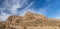 Panoramic of brown Mojave Desert rock formations under a blue sky with white clouds