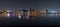 Panoramic cityscape overlooking sea at night with urban lights reflection in water