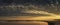 Panoramic cloudscape over the beach at dawn. Curved cove with cormorants on the rocks.