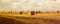 Panoramic image of gold wheat haystacks field at sunset light