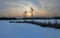 Panoramic image of sunset behind two birches next to a frozen pond in winter