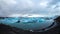 Panoramic of Jokulsarlon glacier lagoon covered with blue icebergs, dramatic landscape, some people walk near the shore