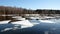 Panoramic landscape with ice floes adrift on the spring river and forest trees on opposite bank under cloudless blue sky on sunny