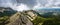 Panoramic landscape of mountain ridge and cloudy gray dramatic sky in the summer.