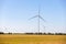 Panoramic landscape view of new white modern wind turbine farm power generation station against clear blue sky and field