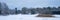 Panoramic landscape view of row of trees in snowy winter forest. Silhouettes of bare trees and evergreens against cold cloudy sky.