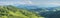 Panoramic mountain view. Peaks in a blue haze, sky, summer greens