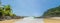 Panoramic photo of Itacarezinho beach, coconut trees, intense vegetation and large stones in encounter with the sea.