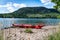 Panoramic photo of red colored kayak stranded on the small Island`s beach and mountain on the other side of the gulf. Red life